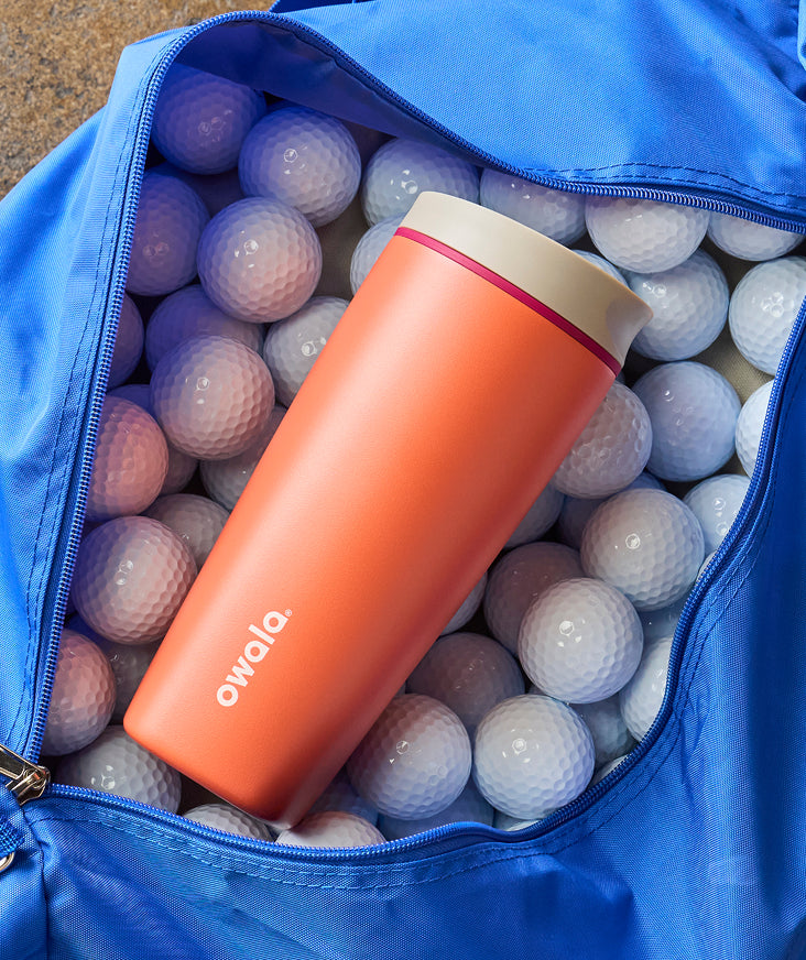 An orange travel mug beside golf balls